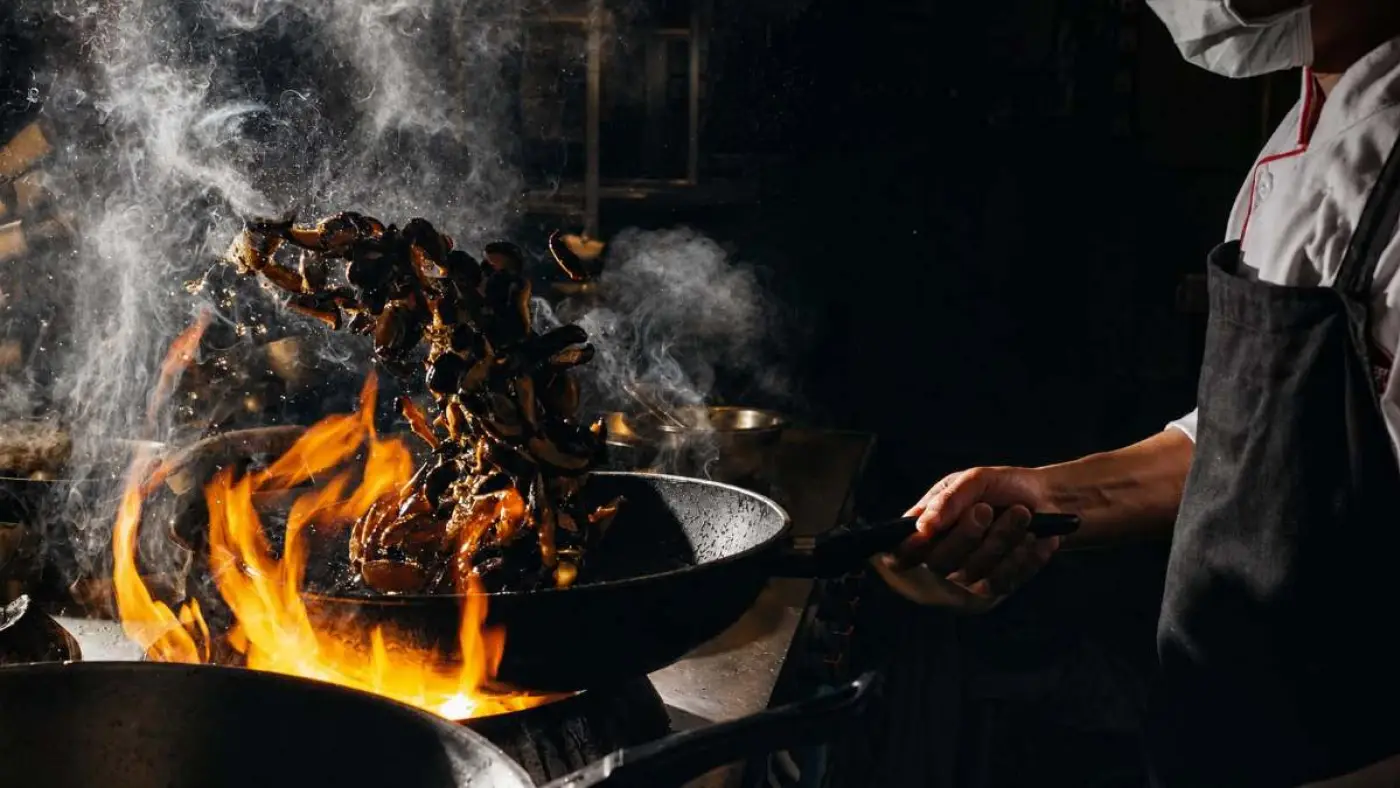 Cozinheiro saltando o alimento sobre a chama, em panela de ferro